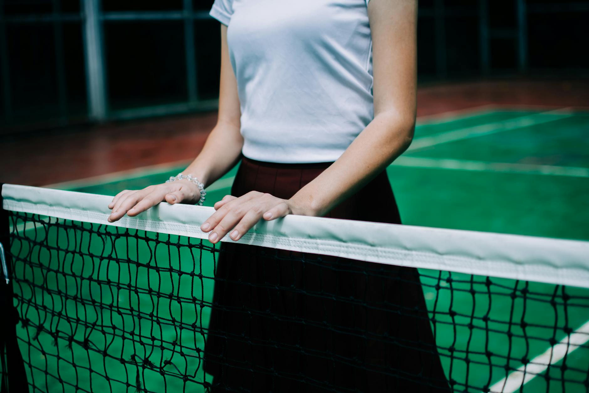 Crop anonymous female in sportswear standing near net ready for tennis play on court