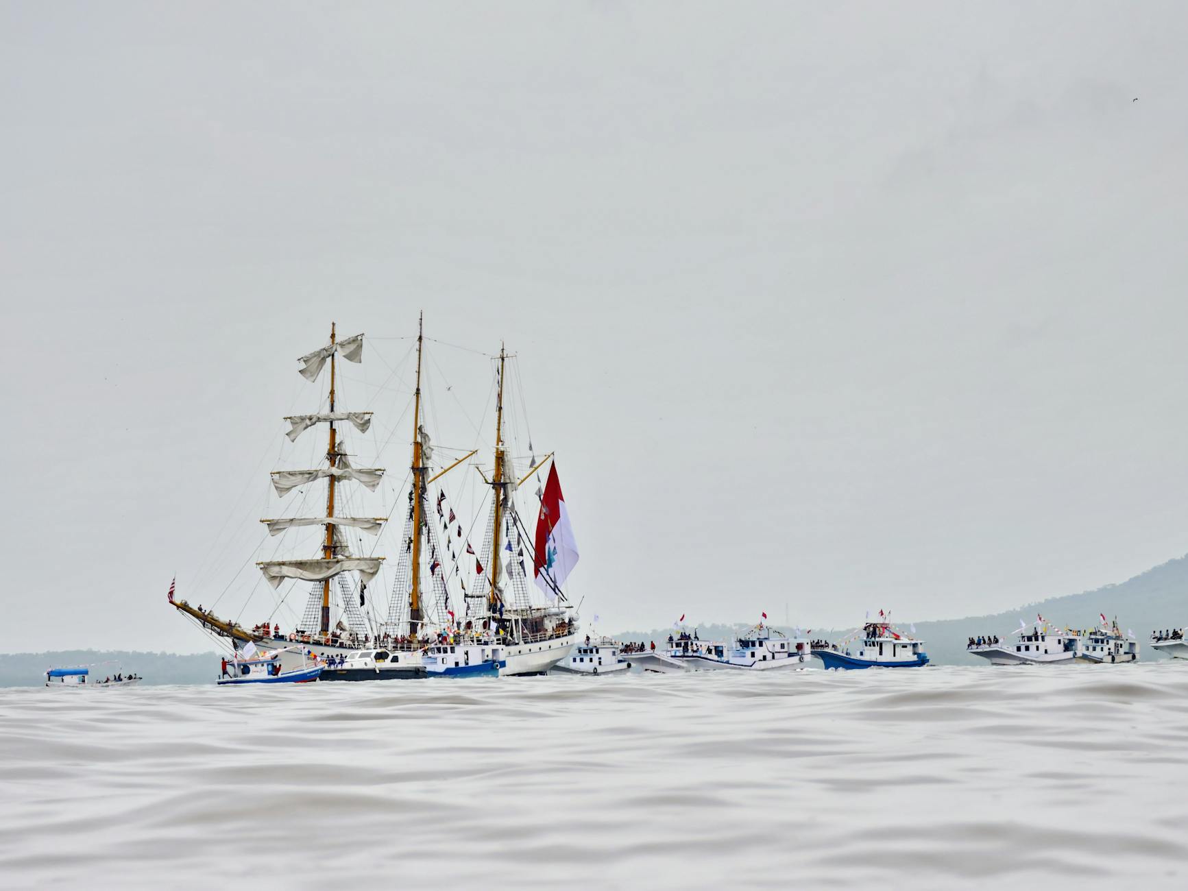 Majestic schooner sailing with escort boats on the open sea capturing the essence of nautical adventure.