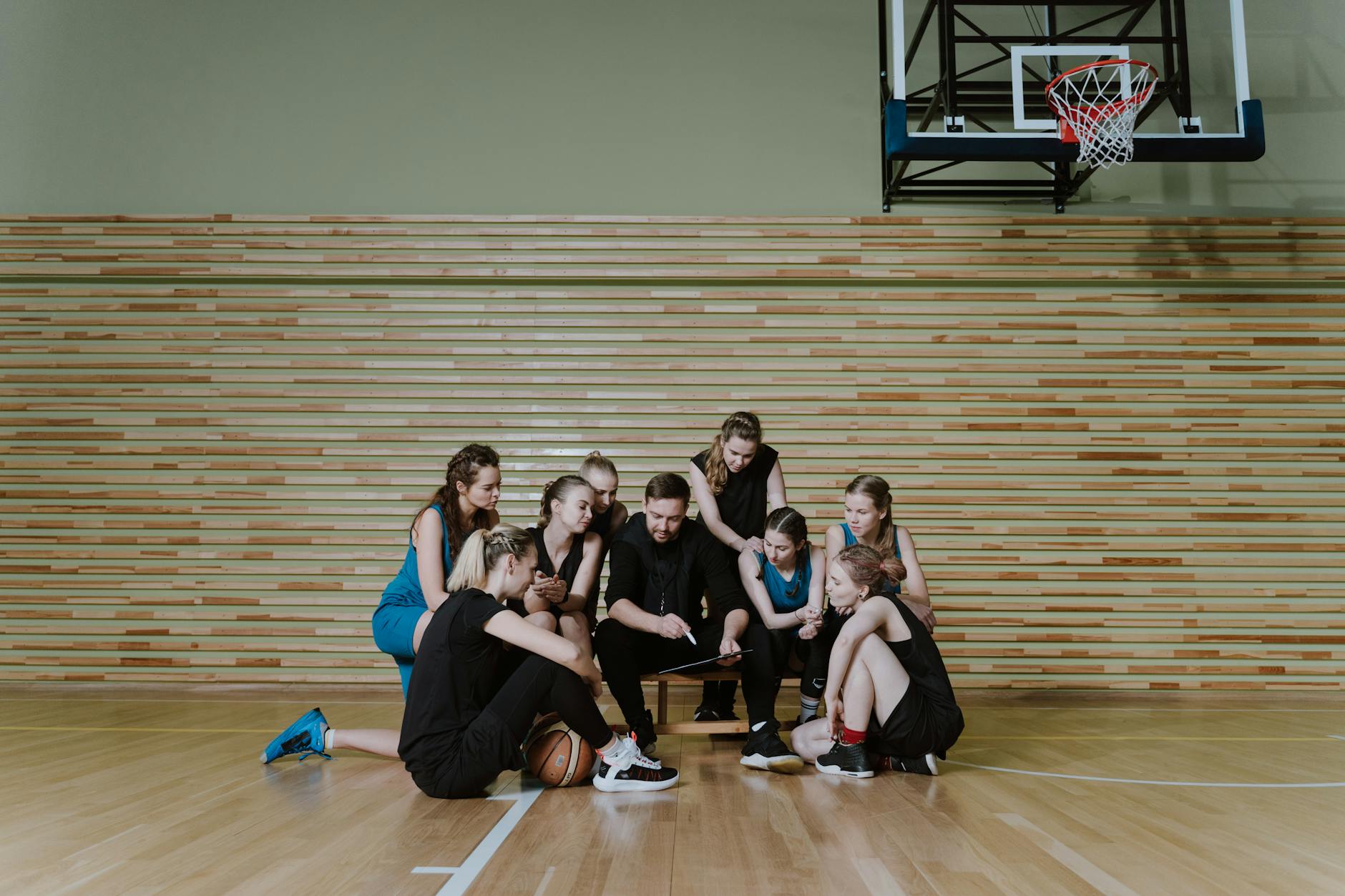 A coach discussing strategies with a female basketball team indoors on a court.
