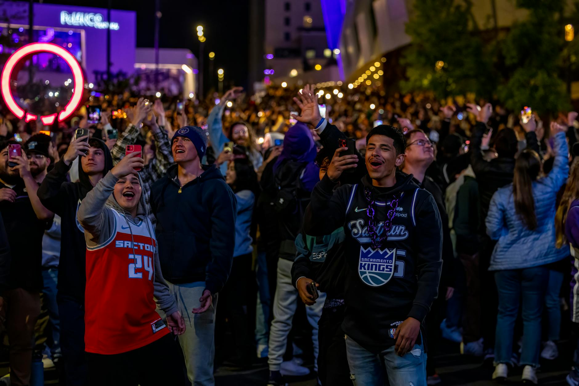 A lively crowd celebrates outdoors at a night event with excitement and joy.