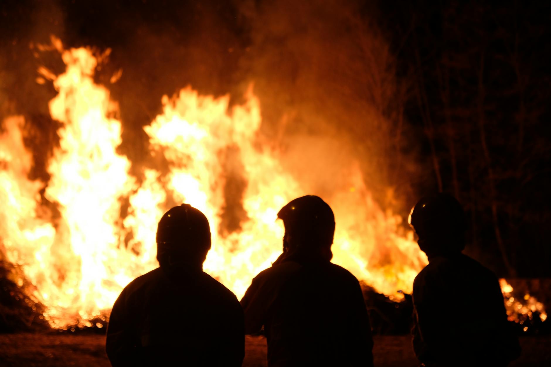 Silhouette of three firefighters watching and managing a large wildfire at night.