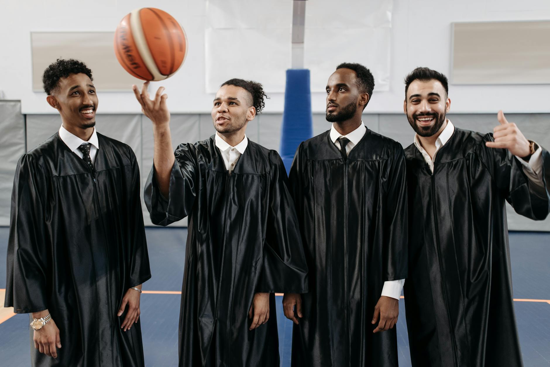 Four young male graduates in gowns enjoying a fun and celebratory moment in a gym.