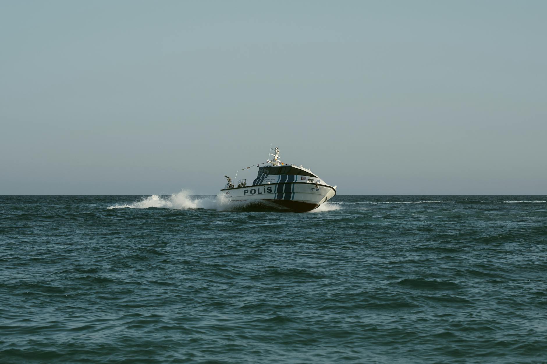 A police boat speeds across the open sea under clear skies, maintaining maritime security.