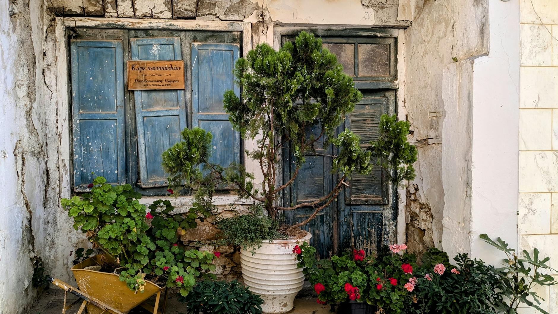 Charming rustic building in Iraklio, Greece with vibrant flowers and blue shutters.