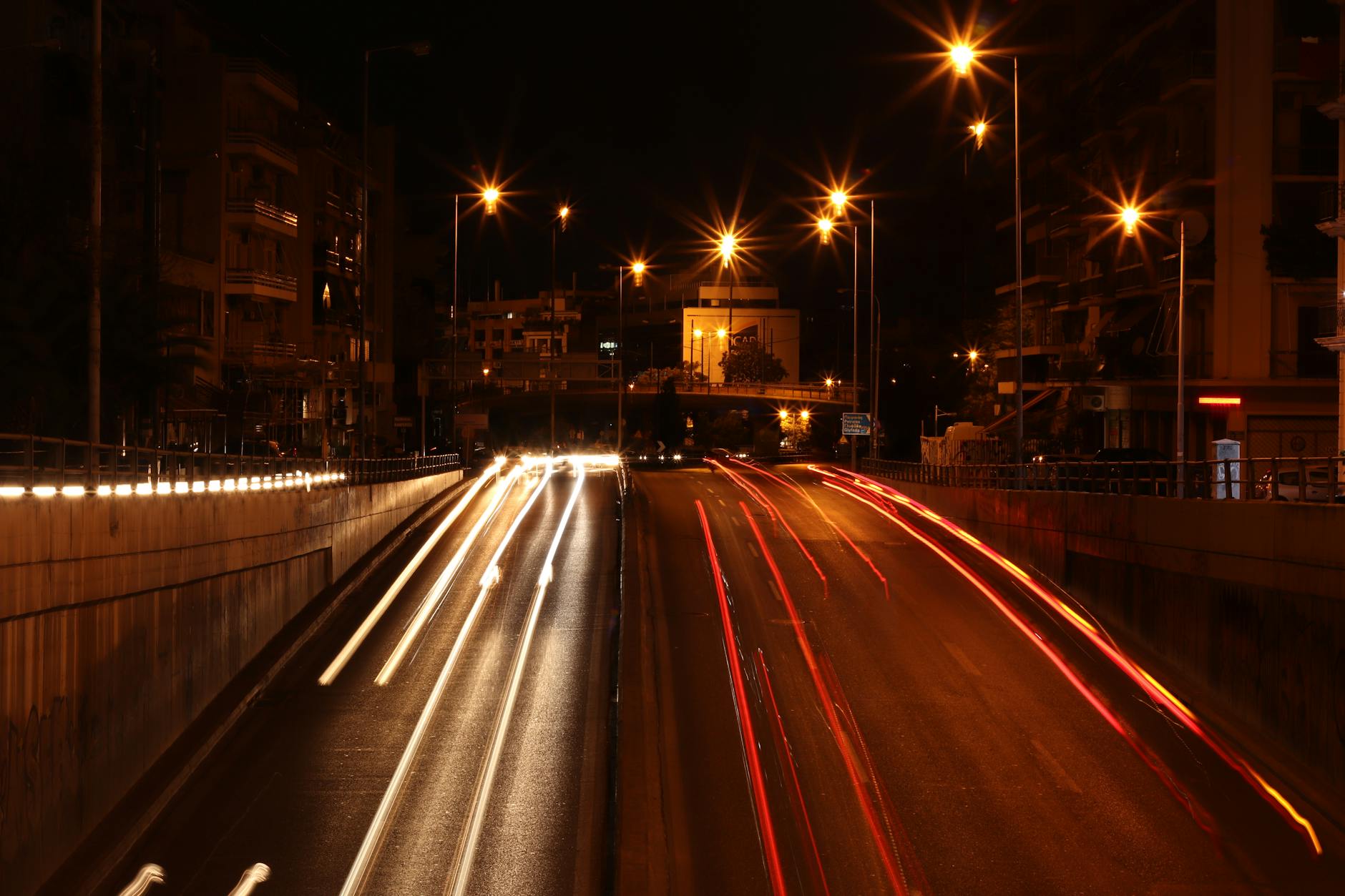 Long exposure of vehicle lights creating trails on a busy Athens road at night.