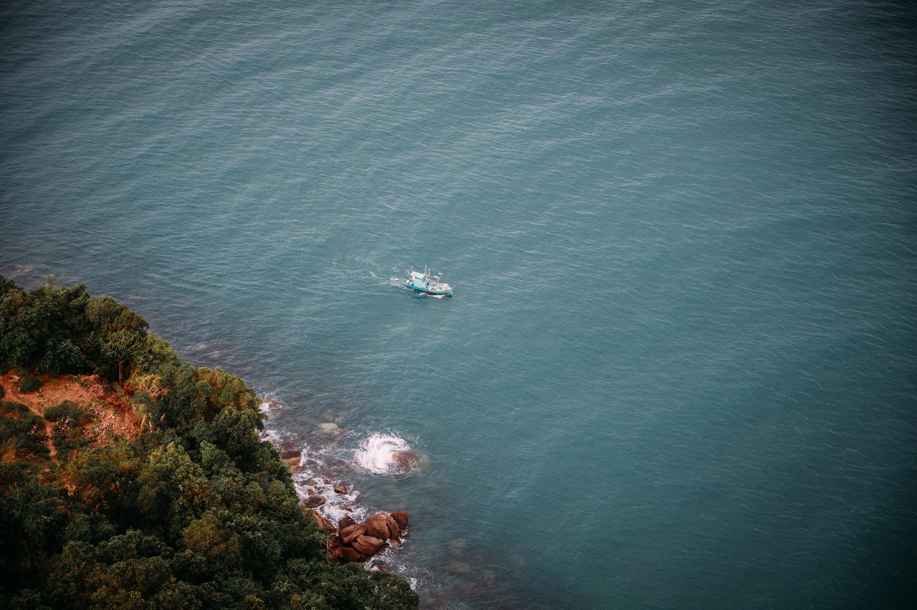 Aerial perspective of a motorboat navigating near a rocky coastline with lush greenery.