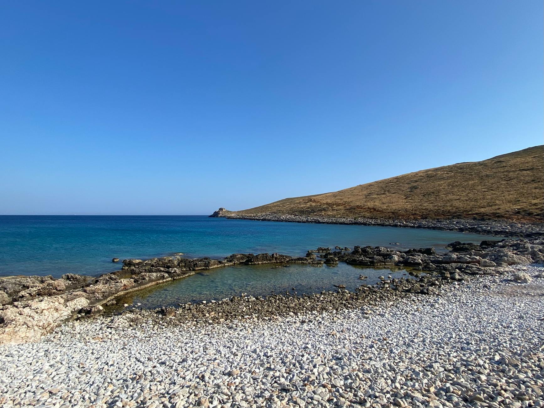 A serene rocky beach in Greece with clear blue waters under a bright sky.